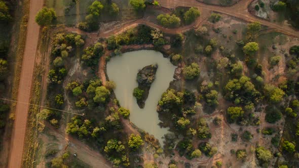small round shaped pond in the middle of african countryside landscape. Bird eyes pull back view