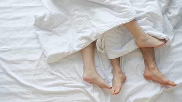 Couple Caresses Each Other Lying in Bed on White Sheets