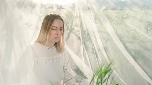 Portrait shot of young woman sitting on grass field in nature surrounded by flying white net during