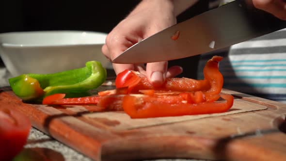 Person Slicing Red Bell Pepper With Knife On Chopping Board In The Kitchen. - close up