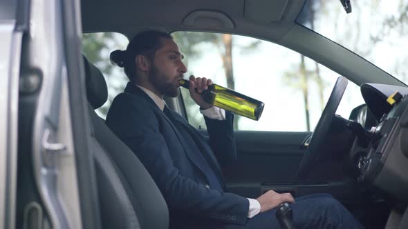 Side View Young Man Sitting on Driver's Seat Drinking From Bottle Looking Away