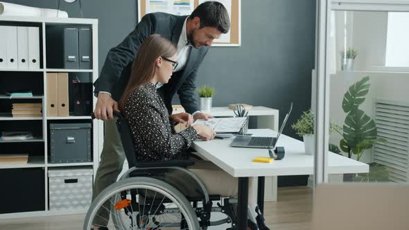 Businesswoman in Wheelchair Talking to Coworker in Office Discussing Business