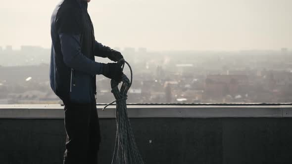 Sports Bald Male Industrial Climber Stands on the Roof of Multi-storey Building and Unties the Rope