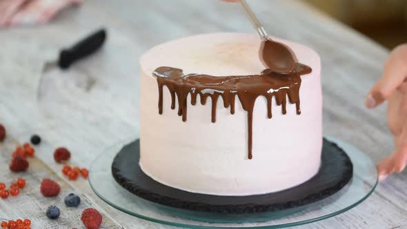 Baker pours liquid chocolate. Confectioner-baker decorate big beautiful cream cake.	