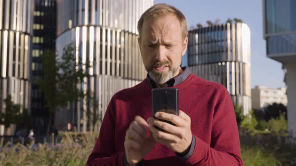 A Middleaged Handsome Caucasian Man Works on a Smartphone Upset in an Urban Area