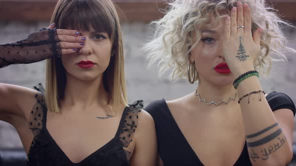 Portrait of Two Serious LGBT Women Looking at Camera Closing One Eye with Hand