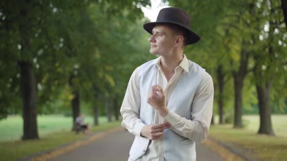 Elegant Handsome Young Man in Hat Walking in Summer Park and Leaving. Portrait of Relaxed Carefree