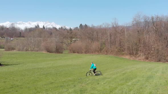 Aerial slow motion: man having fun by riding mountain bike in the grass on sunny day, scenic alpine