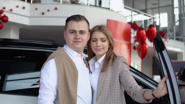 Happy Couple at a Car Dealership with a New Car in the Background