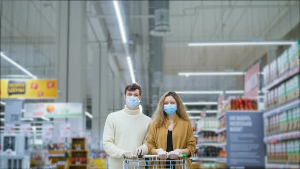 Serious Married Couple in a Medical Mask and Latex Gloves with Grocery Cart Is Standing in