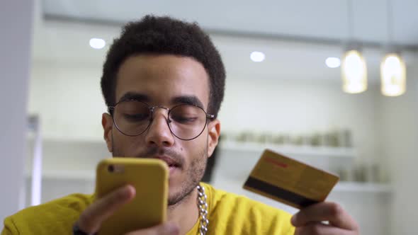 A Young Man Making a Purchase at an Online Store Using a Card and a Smartphone