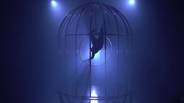 Artist on the Gymnastic Hoop Performs Tricks in a Cage on the Stage in the Dark