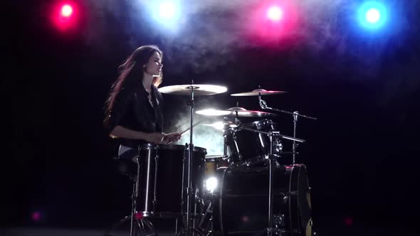 Girl Plays the Drums and Smiles, Black Smoke Background. Red Blue Light From Behind, Side View, Slow