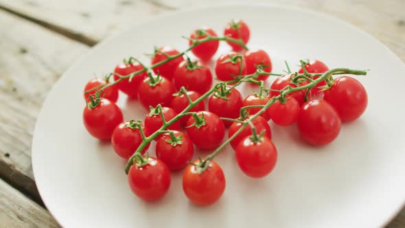 Video of fresh cherry tomatoes on white plate over wooden background