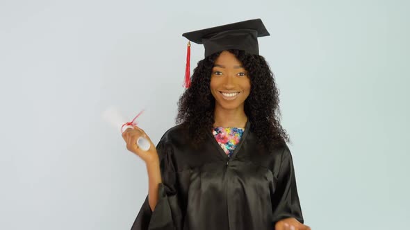 A Young AfricanAmerican Woman in a Black Gown and a Master's Hat Stands Up Straight and Shakes the