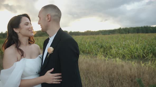 Happy Newlyweds Stand Embracing Near a Cornfield and Talk Looking Into Each Other's Eyes