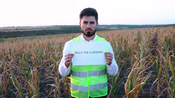 Portrait of a Depressed Young Farmer Holding a Placard in His Hand with the Message HELP THESE