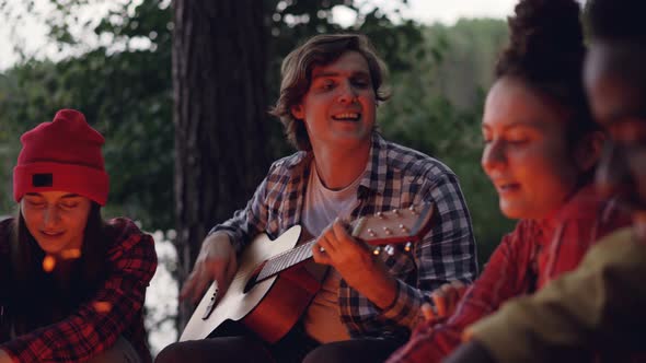 Handsome Young Man Tourist Is Playing the Guitar and Smiling While His Friends Are Singing and