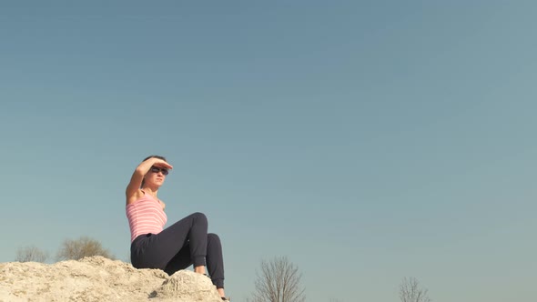 Young Relaxed Woman Sitting Outdoors on a Big Stone Enjoying Warm Summer Day