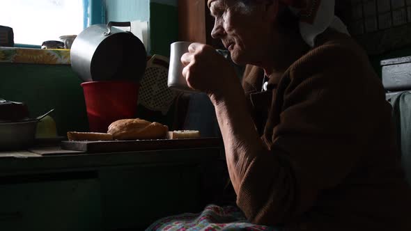 Unhappy wrinkled woman looking in window and chewing bread in loneliness