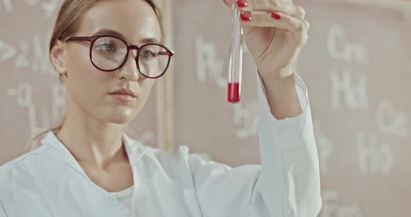 Focused Female Teacher in Lab Coat and Glasses Shaking Red Liquid Substance in Glass Test Tube