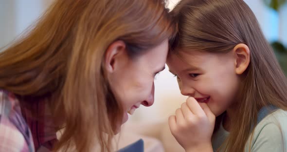 Joyful Mom Sitting with Little Girl on Couch Hugging and Cuddling