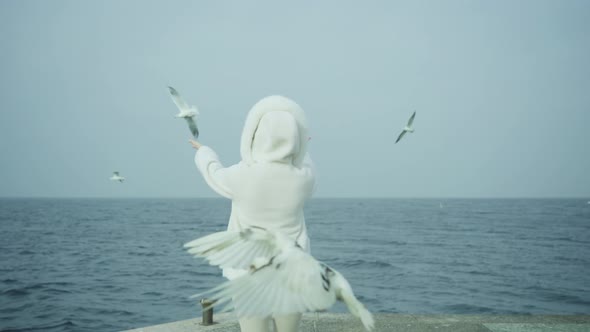 Woman Disperses Birds on Embankment Against Lake Garda