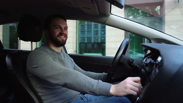 Cheerful bearded young man sitting in car and listens listening to favorite songs