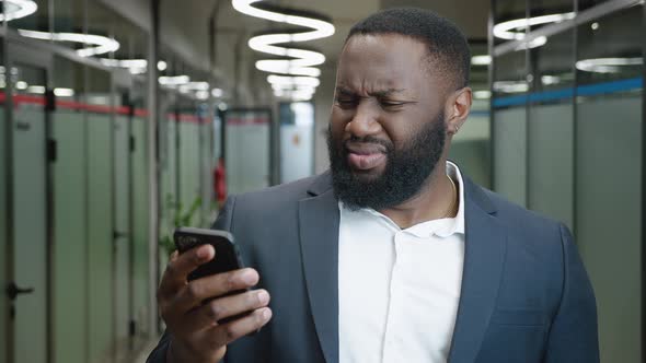 Confused African American Businessman Looks Into a Smartphone