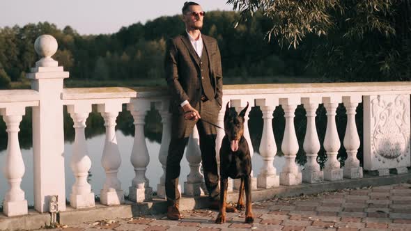 A Rich Businessman in a Business Suit Walks with a Big Doberman in the Park. A Successful Bearded