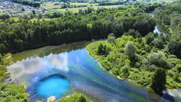 Clouds are reflected in mirror-like transparent lake. Blue deep sinkhole in it