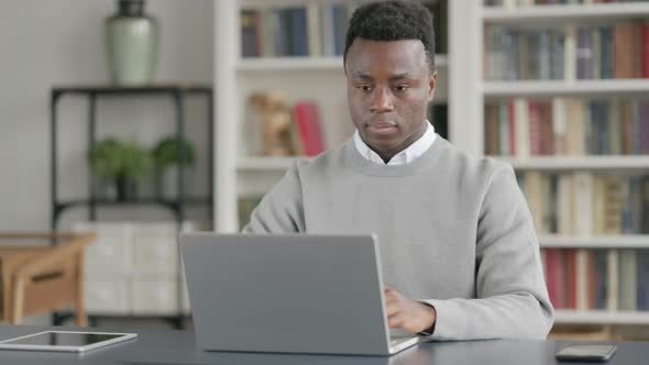 African Man Looking at Camera While Using Laptop in Library