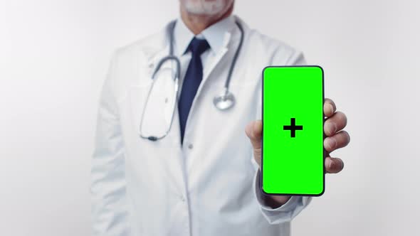 Man Doctor Wearing Glasses with Stethoscope and Medical Robe Holds Phone with Green Screen in His