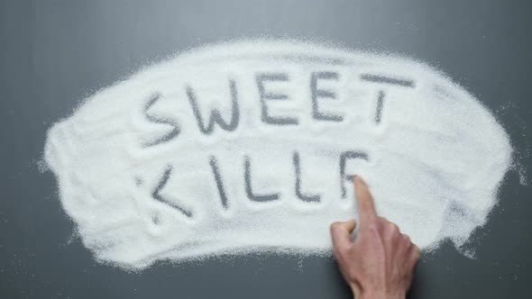 Male hand writes words sweet killer on sugar background. Sugar kills. No sugar.