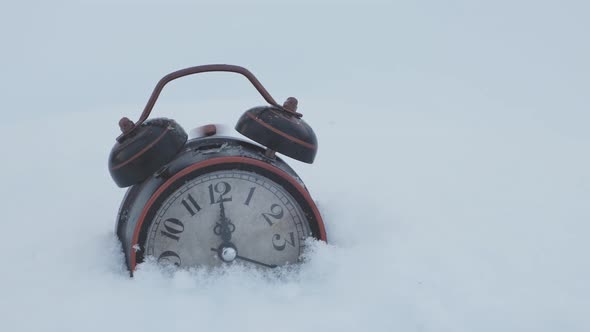 An old alarm clock rings at twelve o'clock, standing in the snow.