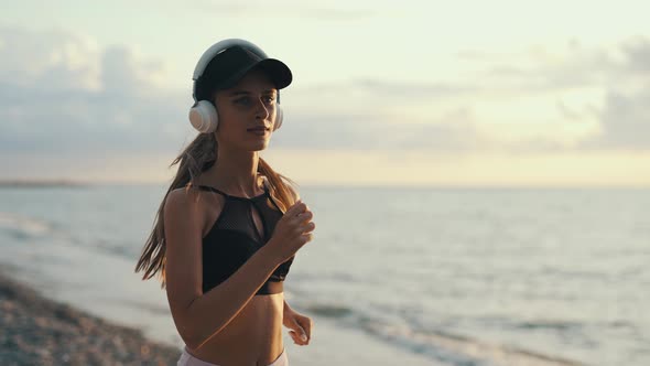 A Young Woman Runner is Listening to Music in Earphones and Training By a Sea