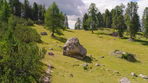 Aerial rising view above boulders in lush woodland at base of South Tyrol Plose Peitlerkofel sunny m