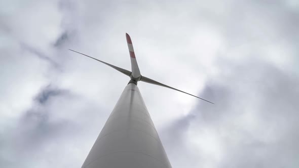 Motion the Blades of a Large Wind Turbine in a Field Against a Background of Cloudy Grey Sky on the