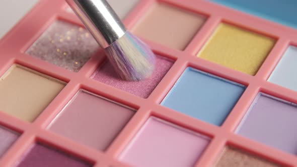 Make-up artist picks up pink pigment from bright colorful eyeshadow palette with a brush.