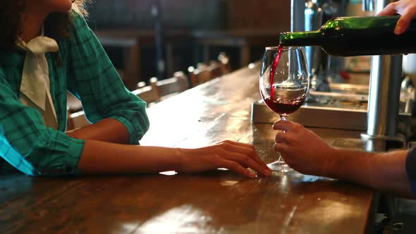Barman serving red wine to female customer at bar counter