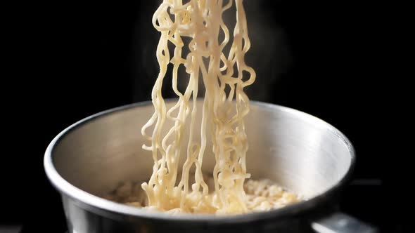 Chopsticks lifting up the instant noodles with steam and smoke in bowl pan. On black background