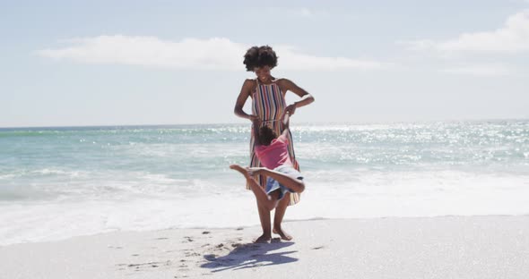 Smiling african american mother with daughter playing on sunny beach