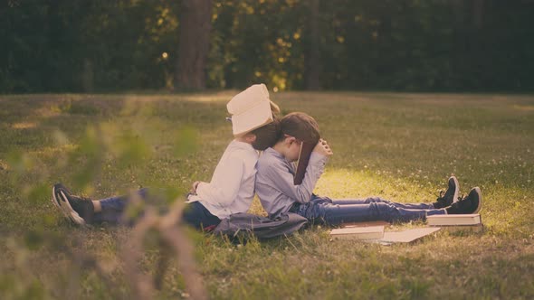 Tired Boys with Textbooks Rest on Lush Lawn Grass in Park