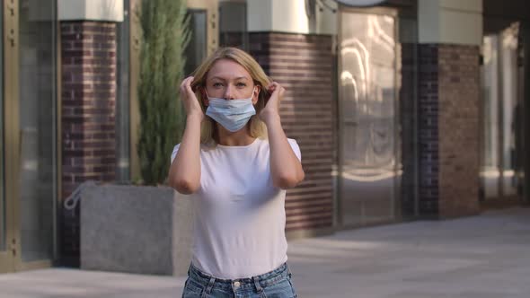 Portrait of Pretty Young Woman Looking Into the Camera and Putting on Medical Mask on Face for