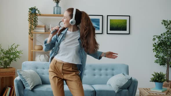 Cute Young Lady Wearing Headphones Dancing and Singing in Remote Control at Home