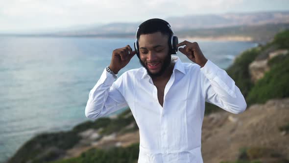 Happy Dance of Joyful Carefree African American LGBTQ Man in Headphones on Mediterranean Sea Coast