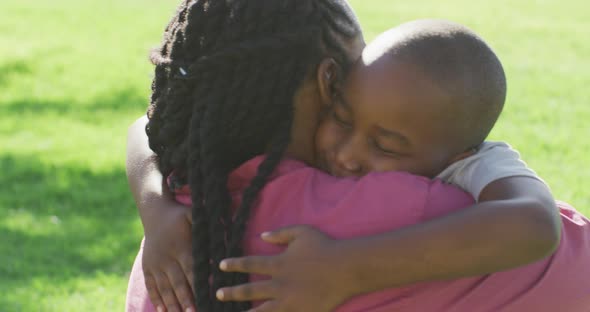 Video of happy african american father and son having picnic on grass and hugging