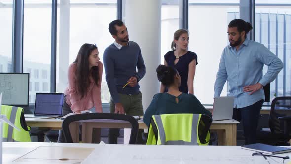 Diverse group of male and female architect colleagues gathered around a table and discussing