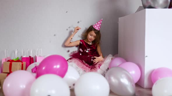 Slow motion beautiful little girl bursting balloon with confetti, having fun at home birthday party.