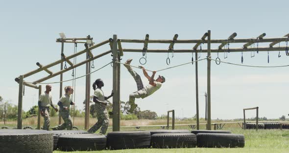 Fit diverse group of soldiers using hanging rope and rings on army obstacle course in the sun